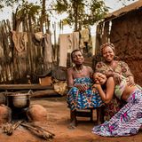 Drei Frauen (Großmutter, Mutter und Tochter) sitzen eng beieinander in Benin auf der Erde