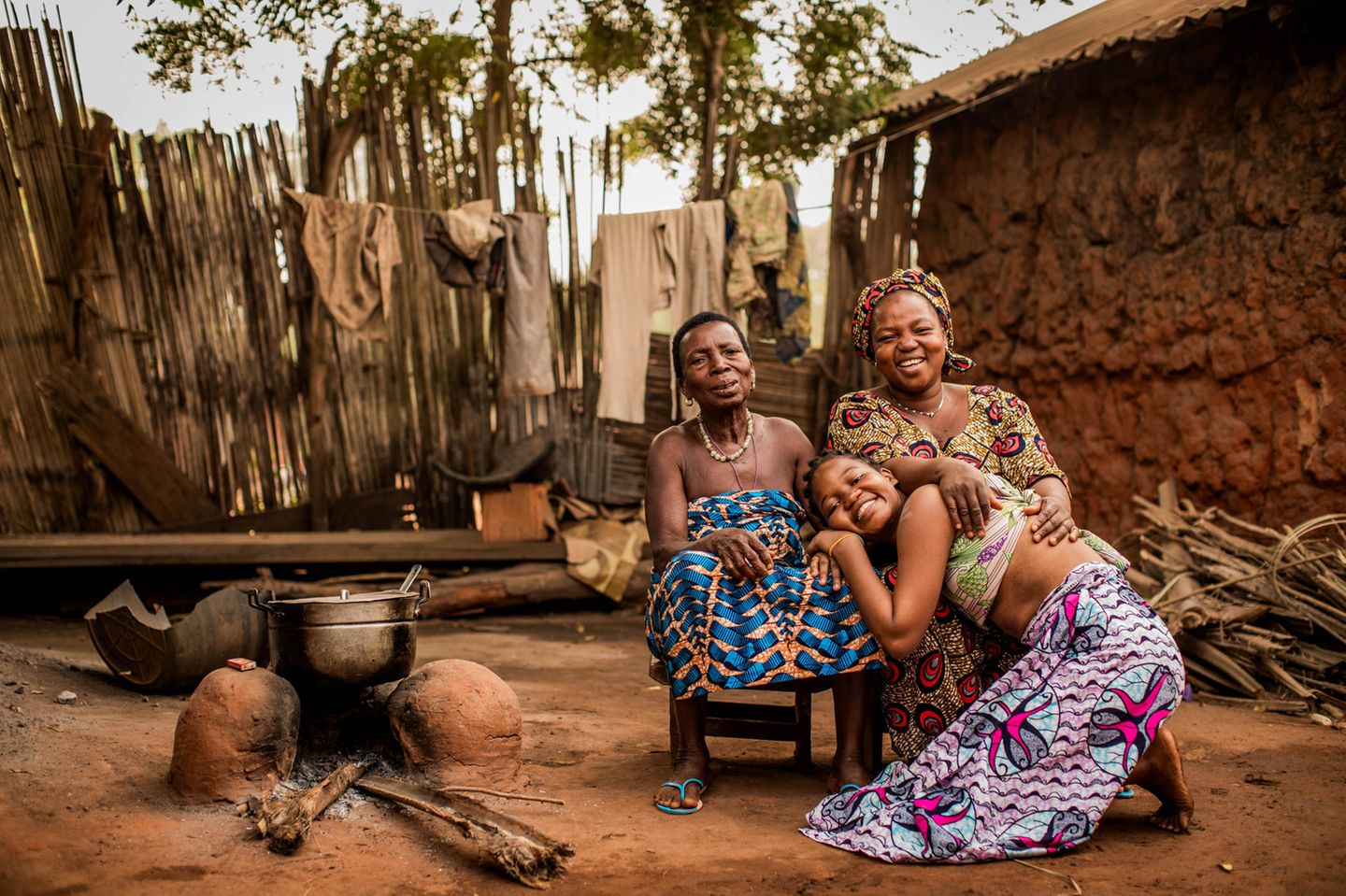 Drei Frauen (Großmutter, Mutter und Tochter) sitzen eng beieinander in Benin auf der Erde