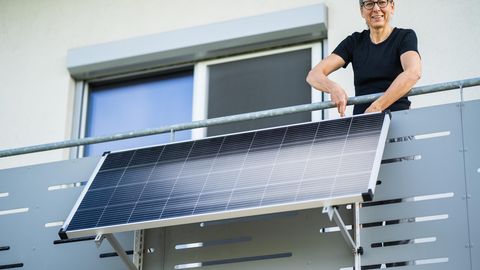 Balkonkraftwerk-Halterung: Frau befestigt ein Solarmodul am Balkongeländer.