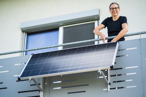 Balkonkraftwerk-Halterung: Frau befestigt ein Solarmodul am Balkongeländer.