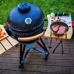 Keramikgrills: Kamado steht auf einer Terrasse, Fleisch und Gemüse auf dem Beistelltisch