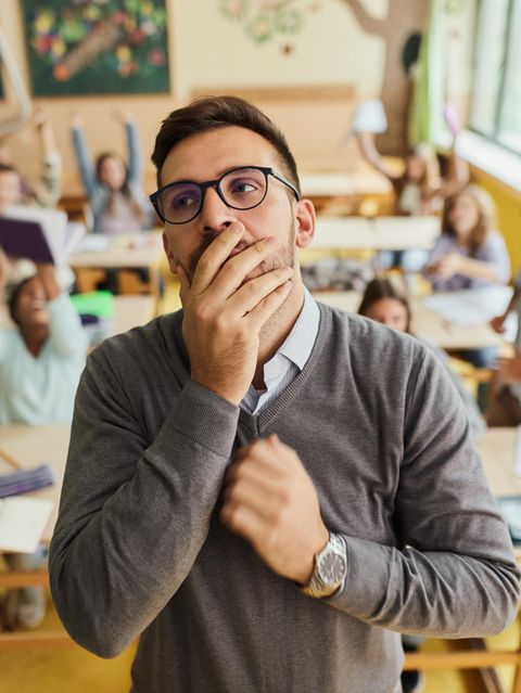 Lehrer mit Hand vor dem Mund vor unruhiger Schulklasse, in Deutschland herrscht Lehrermangel