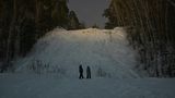 Zwei Gestalten im dunkel vor einem schneebedeckten Hügel.