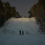 Zwei Gestalten im dunkel vor einem schneebedeckten Hügel.