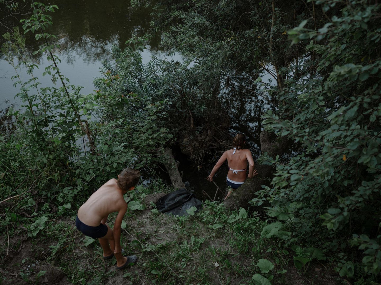 Zwei Kinder steigen in Badekleidung in die Böschung an einem Fluss