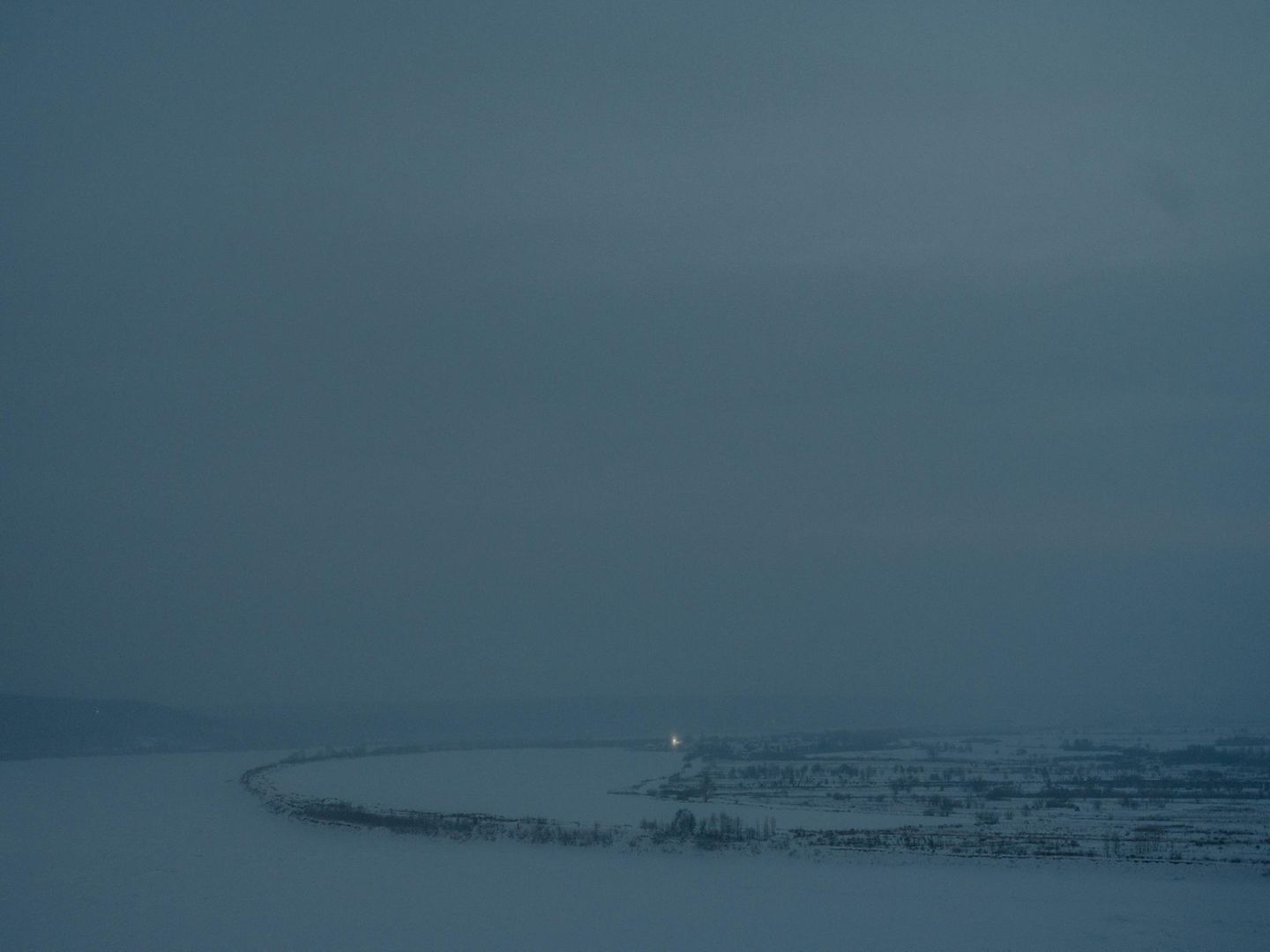 Eine Landschaft im Schnee. Es dringt kaum Licht durch die Wolken.