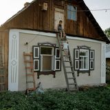 Zwei Kinder sind auf eine Leiter geklettert, die an einer Hauswand lehnt.