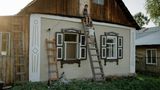 Zwei Kinder sind auf eine Leiter geklettert, die an einer Hauswand lehnt.