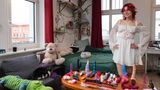 Junge Frau in weißem Kleid mit Elfenohren posiert in ihrer eigenen Wohnung vor ihrer Sammlung von Sexspielzeugen