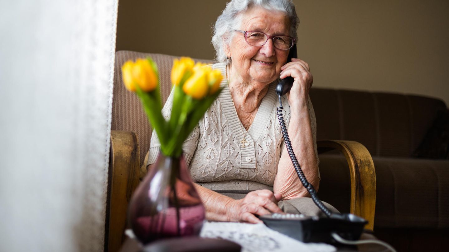 Eine ältere Frau nutzt ein Festnetztelefon – zum Beispiel, um die Auskunft anzurufen