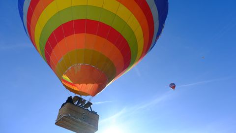 Ein horizontal gestreifter Heißluftballon hebt sich vom strahlend blauen Himmel ab