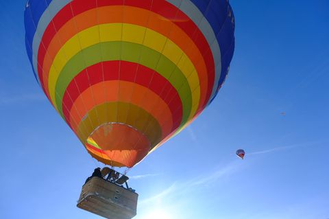 Ein horizontal gestreifter Heißluftballon hebt sich vom strahlend blauen Himmel ab