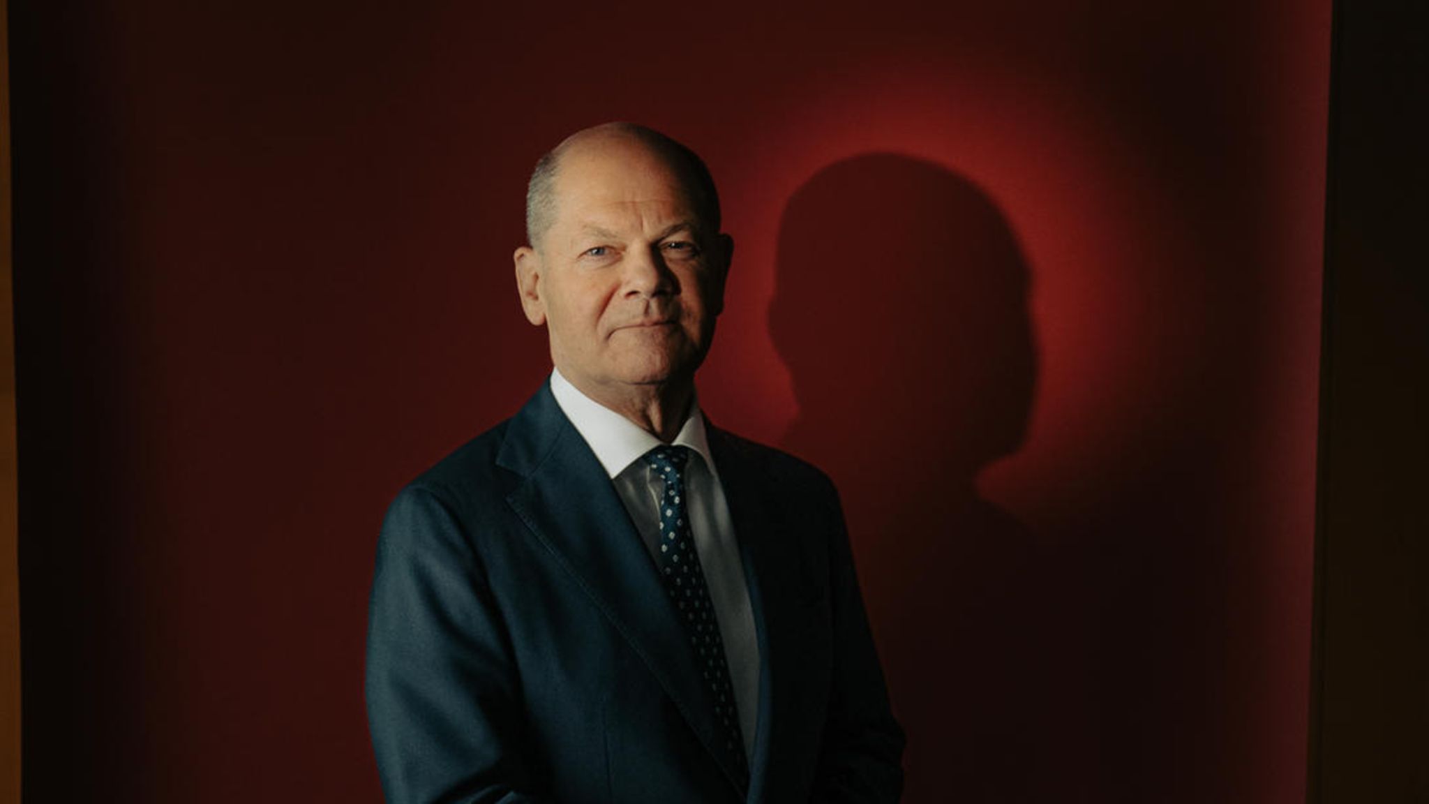 Portrait von Olaf Scholz vor rotem Hintergrund mit gefalteten Händen