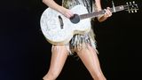 Taylor Swift in einem silbrig glänzenden Fransenkleid mit Gitarre