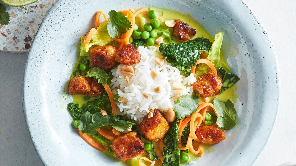 Wirsing-Curry mit Tofu-Bites  Für 4 Personen     TOFU-BITES  400 g Tofu  3 El Speisestärke  Salz  3 El Rapsöl (ersatzweise Kokosöl)     CURRY  30 g frischer Ingwer ∙3 Knoblauchzehen ∙15 g Zitronengras ∙2 El Kokosöl  2 Tl gemahlene Kurkuma  3 Tl gemahlener Koriander  3 Tl vegane grüne Currypaste  (z. B. von Bamboo Garden) ∙2 Tl Currypulver  1 l ungesüßte Kokosmilch   1 Kaffirlimettenblatt  Salz   240 g Jasminreis  1⁄2 Wirsing (450 g)  4 Möhren (à 125 g)  200 g TK-Erbsen (aufgetaut)     MARINADE UND TOPPING  3 Limetten  4 El Agavendicksaft  1 El Sojasauce  2 Tl edelsüßes Paprikapulver ∙1 Tl rosenscharfes Paprikapulver  1 Tl gemahlene Koriandersaat  1 Tl gemahlener Kreuzkümmel  1/2 Tl Chiliflocken  4 Stiele Koriandergrün ∙1 Handvoll geröstete und  gesalzene Erdnüsse     Zubereitung:  1. Für die Tofu-Bites Tofu abtropfen lassen, in ein sauberes Geschirrtuch einschlagen, auf einen flachen Teller legen, mit einem Topf beschweren und mindestens 20 Minuten pressen.  2. Inzwischen für das Curry Ingwer schälen und mit Knoblauch fein reiben. Zitronengras putzen, die äußeren harten Schichten entfernen. Stange mit einem Messerrücken andrücken und fein schneiden. Kokosöl in einem großen Topf (oder Wok) erhitzen. Zitronengras, Knoblauch und Ingwer 2 Minuten darin andünsten. Kurkuma, Koriander, Currypaste und -pulver zugeben und  3—4 Minuten mitdünsten. Kokosmilch zugießen und aufkochen. Limettenblatt zugeben, alles bei kleiner Hitze 10 Minuten kochen lassen. Limettenblatt entfernen. Curry mit dem Stabmixer fein pürieren und mit Salz würzen.  3. Reis in kochendem Salzwasser nach Packungsanweisung garen, abgießen, abtropfen lassen und warm stellen. Wirsing putzen und den Strunk entfernen. Wirsing längs vierteln und in 2 cm breite Streifen schneiden. Wirsingstreifen in kochendem Salzwasser 2—3 Minuten blanchieren, in Eiswasser abschrecken und abtropfen lassen. Möhren putzen, schälen und mit einem Sparschäler längs in dünne Streifen schneiden. Möhren, Erbsen und Wirsing zum Curry geben. 3 Minuten bei mittlerer Hitze kochen und zugedeckt warm stellen.  4. Für die Tofu-Bites gepressten Tofu in 1—2 cm große Stücke brechen. Stärke und 1⁄2 Tl Salz in einer flachen Schale mischen. Tofu darin wälzen, sodass er rundum ummantelt ist. Öl in einer beschichteten Pfanne erhitzen. Tofu darin bei mittlerer bis starker Hitze 8—10 Minuten braten, dabei gelegentlich wenden.  5. Für die Marinade Limetten halbieren, 75 ml Saft auspressen und mit Agavendicksaft, Sojasauce und Gewürzen verrühren. Zum Tofu in die Pfanne geben, zügig umrühren und 2 Minuten glasieren. Reis und Curry in tiefen Tellern anrichten. Mit Tofu, abgezupften Korianderblättern und Nüssen bestreut servieren.