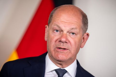 Olaf Scholz steht im Anzug vor einer deutschen Flagge
