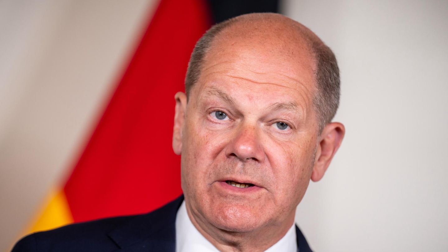 Olaf Scholz steht im Anzug vor einer deutschen Flagge