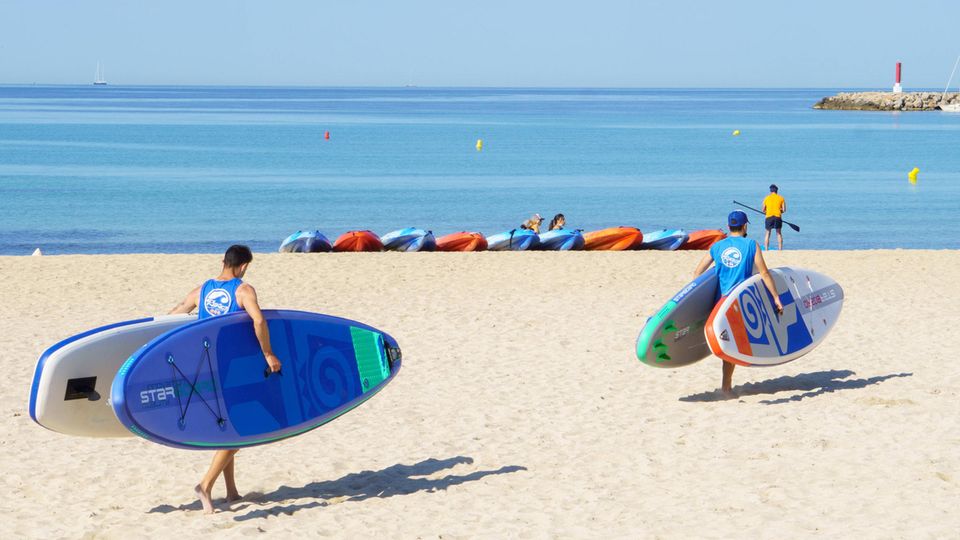Männer tragen SUP-Boards über einen Strand