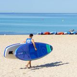 Männer tragen SUP-Boards über einen Strand