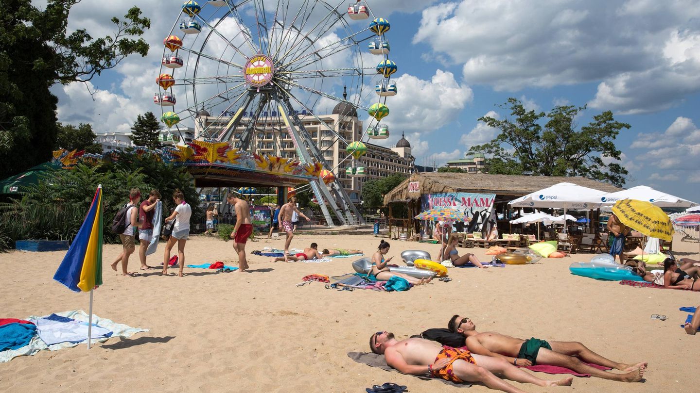 Menschen liegen an einem Strand, im Hintergrund ist ein Riesenrad zu sehen