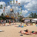 Menschen liegen an einem Strand, im Hintergrund ist ein Riesenrad zu sehen