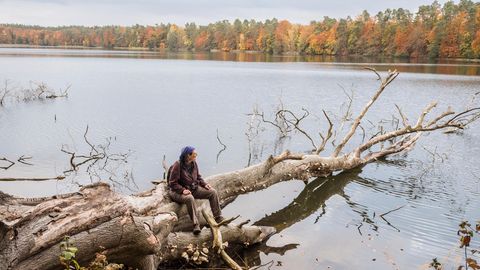 Christine Thuermer sitzt auf einem alten Baum der in einen See hinein ragt und schaut auf das Wasser