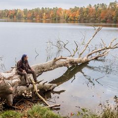 Christine Thuermer sitzt auf einem alten Baum der in einen See hinein ragt und schaut auf das Wasser