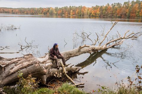 Christine Thuermer sitzt auf einem alten Baum der in einen See hinein ragt und schaut auf das Wasser