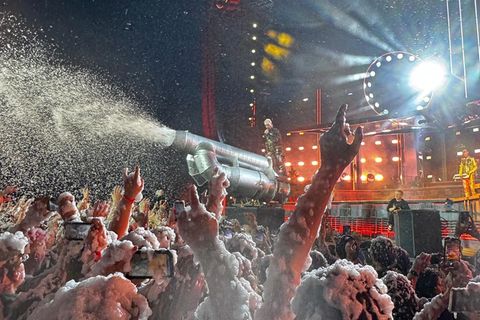 Rammstein Frontmann Till Lindemann steht an einem Gerät, das Scham auf sein Publikum spritzt