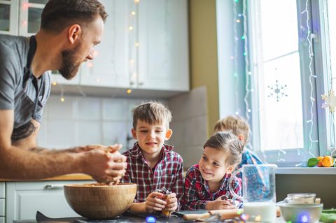 Tagesvater: Ein Mann zeigt Kindern in der Küche wie man einen Teig knetet. Die Kinder schauen zu.