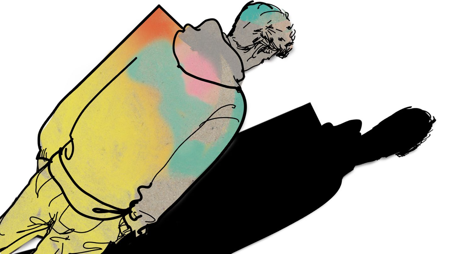 Ein junger Mann steht schräg mit dem Rücken zu uns. Eine Schulter ist eckig.