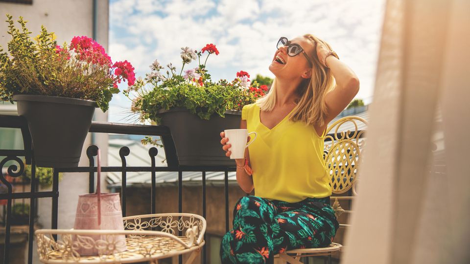 Junge Frau genießt die Sonne auf romantischem Balkon mit Blumenkästen