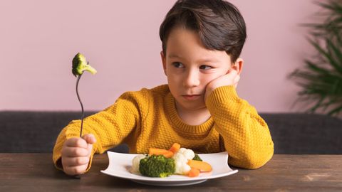 Essstörung ARFID bei Kindern: Ein kleiner Junge sitzt vor einem Teller mit Gemüse