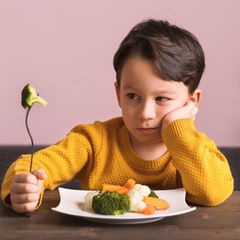 Essstörung ARFID bei Kindern: Ein kleiner Junge sitzt vor einem Teller mit Gemüse