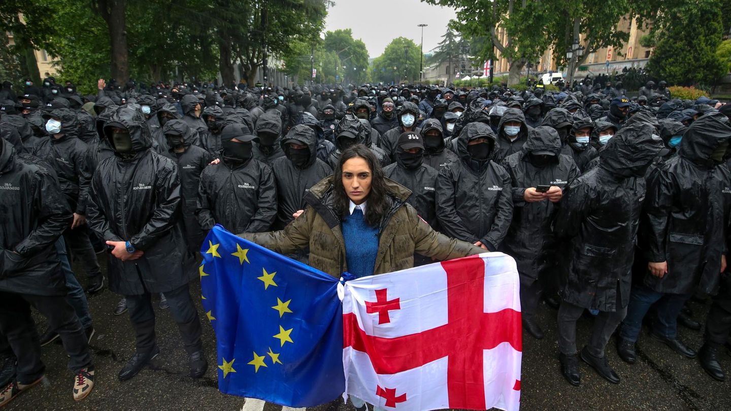 Wochenlange Proteste: Eine Frau demonstriert in Georgiens Hauptstadt Tiflis mit der Landes- und der EU-Flagge anlässlich der Verabschiedung des Gesetzes zur "Transparenz ausländischer Einflussnahme" am vergangenen Dienstag. Im Hintergrund sperren Polizisten eine Straße ab. Eine Frau demonstriert in Georgiens Hauptstadt Tiflis mit der Landes- und der EU-Flagge anlässlich der Verabschiedung des Gesetzes zur "Transparenz ausländischer Einflussnahme" am vergangenen Dienstag. Im Hintergrund sperren Polizisten eine Straße ab.