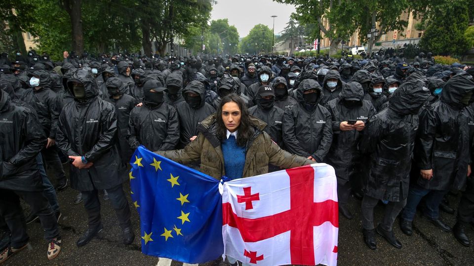 Eine Frau demonstriert in Georgiens Hauptstadt Tiflis mit der Landes- und der EU-Flagge anlässlich der Verabschiedung des Gesetzes zur "Transparenz ausländischer Einflussnahme" am vergangenen Dienstag. Im Hintergrund sperren Polizisten eine Straße ab.
