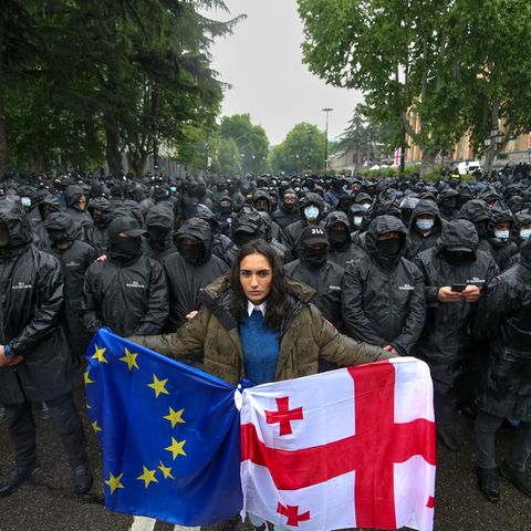 Eine Frau demonstriert in Georgiens Hauptstadt Tiflis mit der Landes- und der EU-Flagge anlässlich der Verabschiedung des Gesetzes zur "Transparenz ausländischer Einflussnahme" am vergangenen Dienstag. Im Hintergrund sperren Polizisten eine Straße ab.