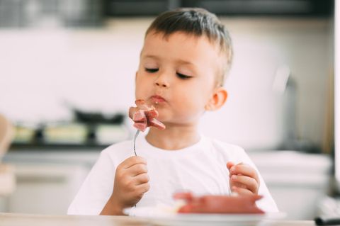 Ein Junge blickt kritisch auf seine Gabel mit Fleisch