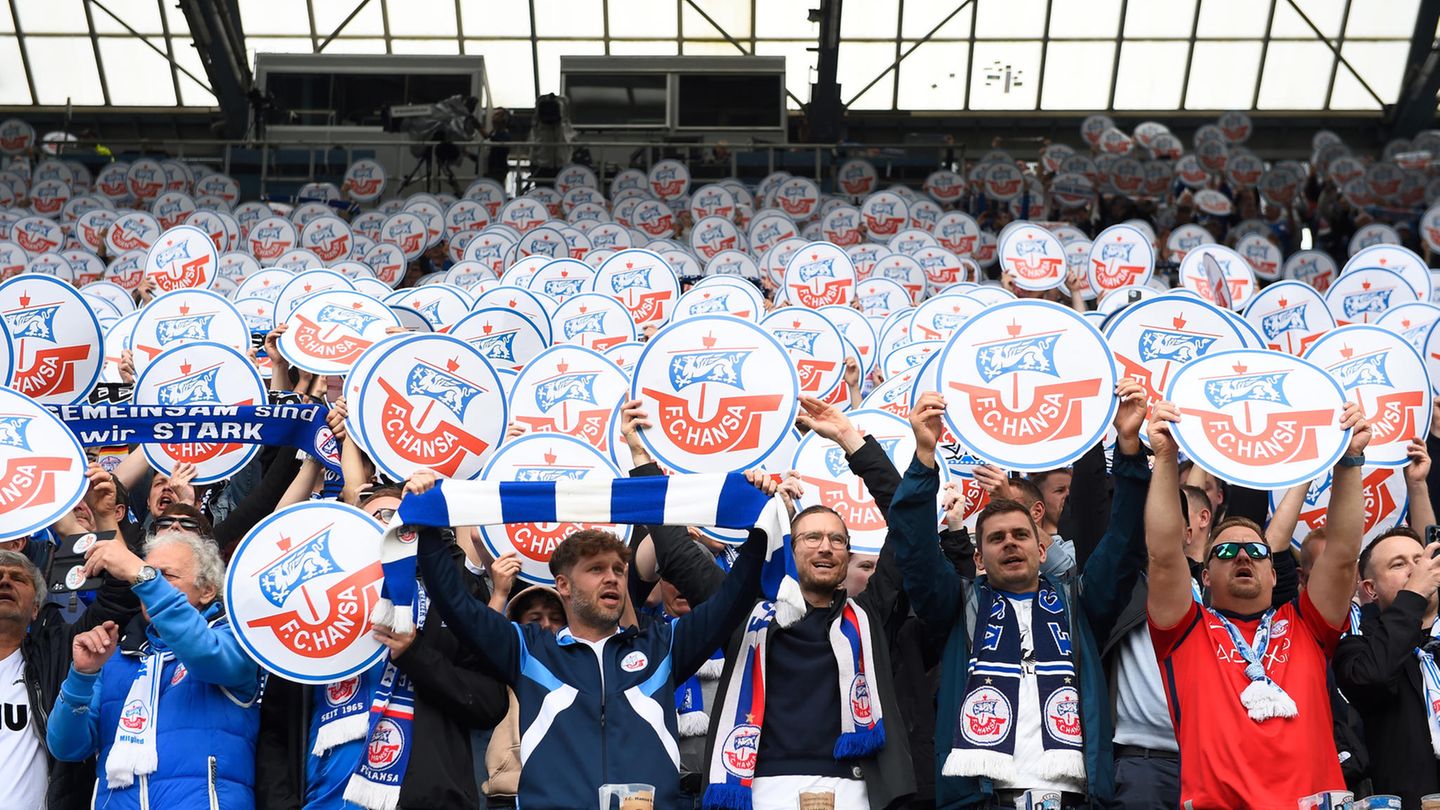 Fans des FC Hansa Rostock halten vor Spielbeginn Schilder mit dem Vereinslogo auf der Tribüne in die Höhe.