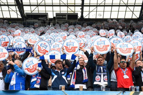 Fans des FC Hansa Rostock halten vor Spielbeginn Schilder mit dem Vereinslogo auf der Tribüne in die Höhe.