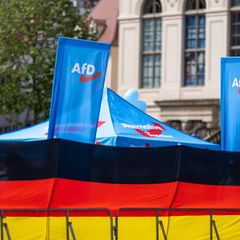 Eine Deutschland Flagge und dahinter ein Wahlstand der AfD