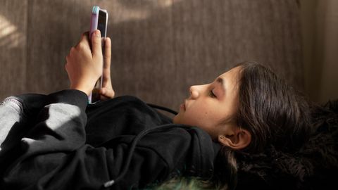 Ein Kind liegt auf dem Rücken und hält ein Smartphone