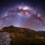 Eine violette Milchstraße über felsigem Gelände mit einer kleinen beleuchteten Hütte