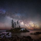 Eine kleine Insel mit ein paar Tannen in einem See die Milchstraße als eine lange leuchtende Linie im Nachthimmel