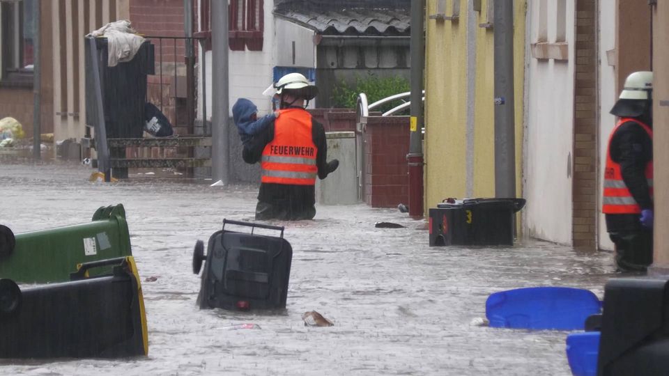 Ein freiwilliger Helfer watet durch das Hochwasser und trägt eine Person.