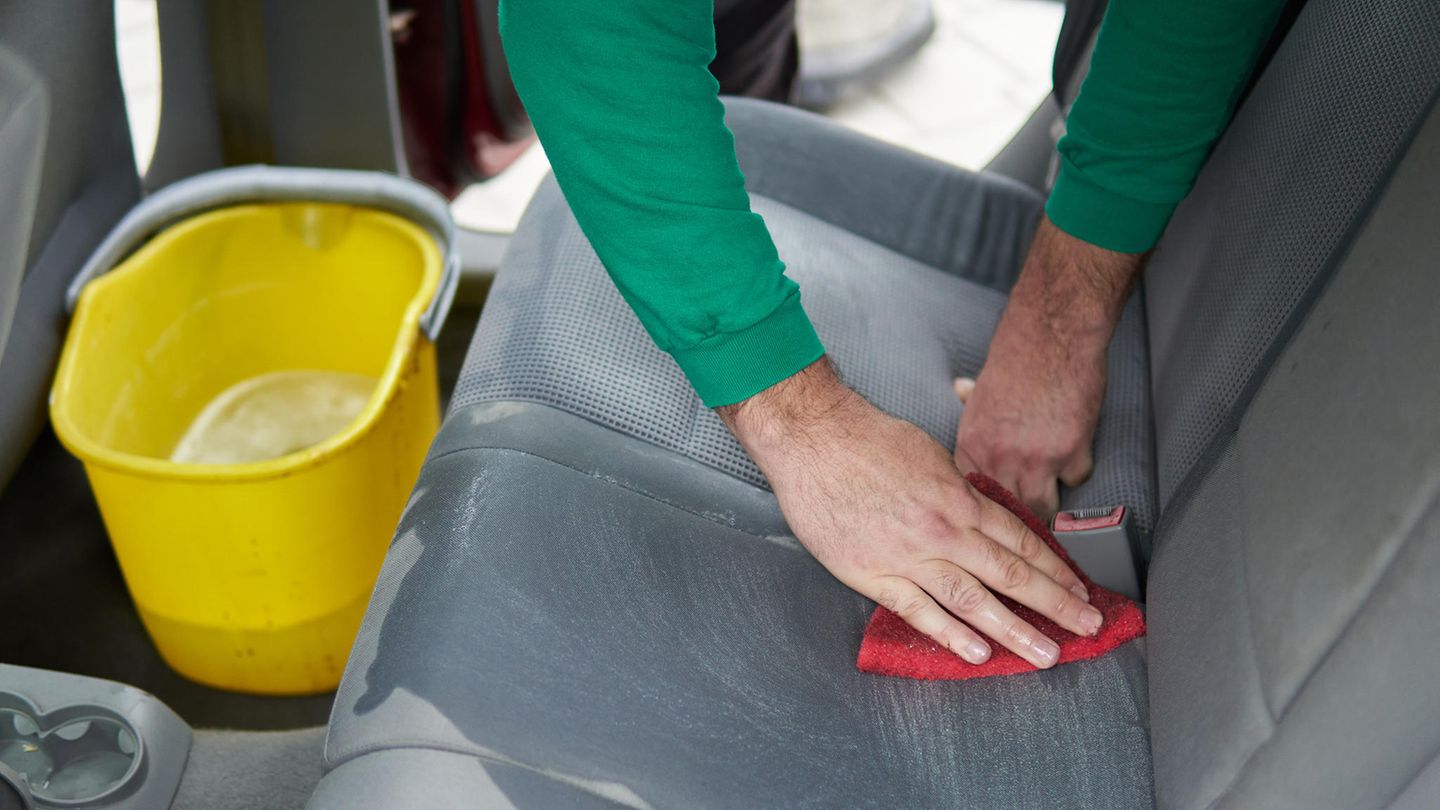 Autositze reinigen: Mann säubert mit einem roten Lappen die Sitzpolster