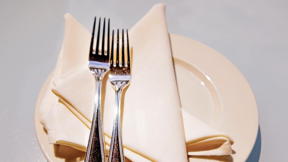 Zwei Gabeln liegen auf gefalteten Servietten auf einem Teller