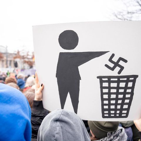 Auf einer Demonstration hält ein Teilnehmer ein Plakat hoch, auf dem das nationalsozialistische Symbol im Müll verschwindet.