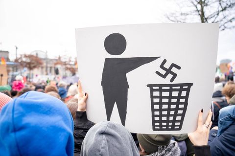 Auf einer Demonstration hält ein Teilnehmer ein Plakat hoch, auf dem das nationalsozialistische Symbol im Müll verschwindet.