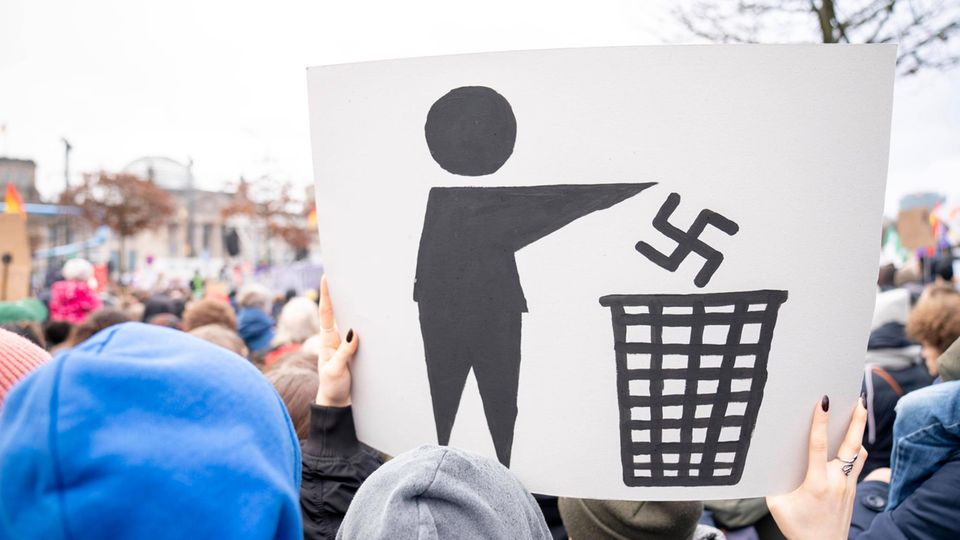 Auf einer Demonstration hält ein Teilnehmer ein Plakat hoch, auf dem das nationalsozialistische Symbol im Müll verschwindet.